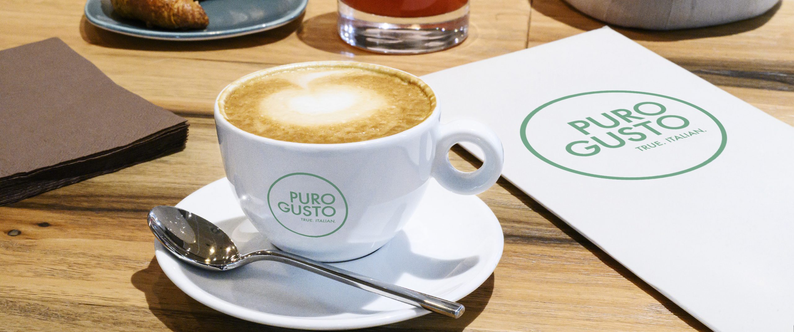 A coffee cup and a menu with the Puro Gusto Logo on a table.